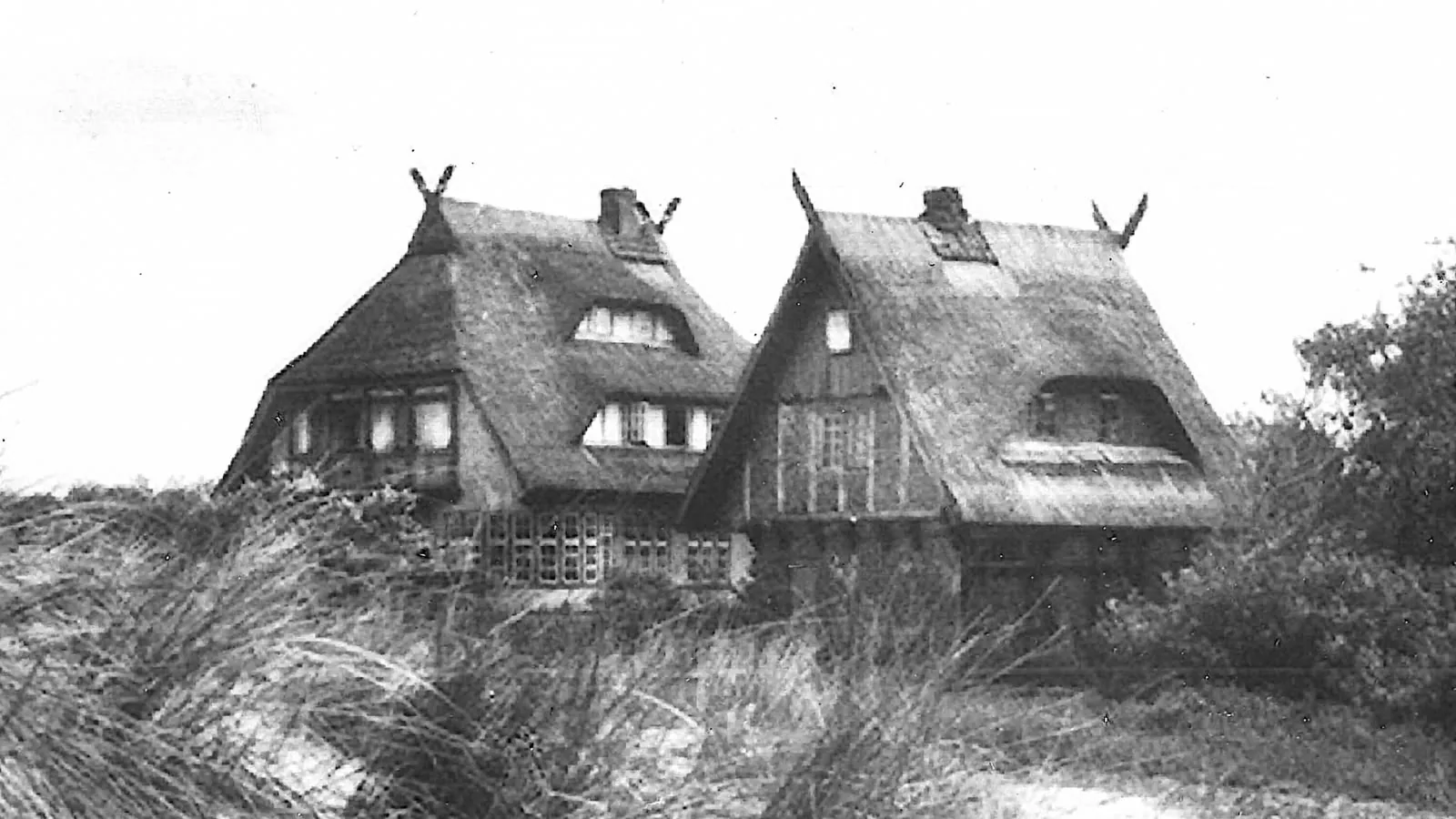 Haus Windhook mit zwei Reetdachgiebeln und gekreuzten Giebelsparren, eingebettet ins Dünengras – historische Aufnahme